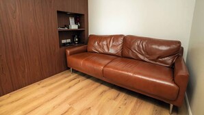 A brown leather sofa against a wooden wall with a shelf containing a coffee maker and a vase. - Play Poshtel & Cafe (Krabi)