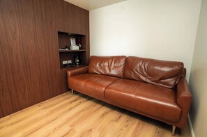 A brown leather sofa against a wooden wall with a shelf containing a coffee maker and a vase. - Play Poshtel & Cafe (Krabi)