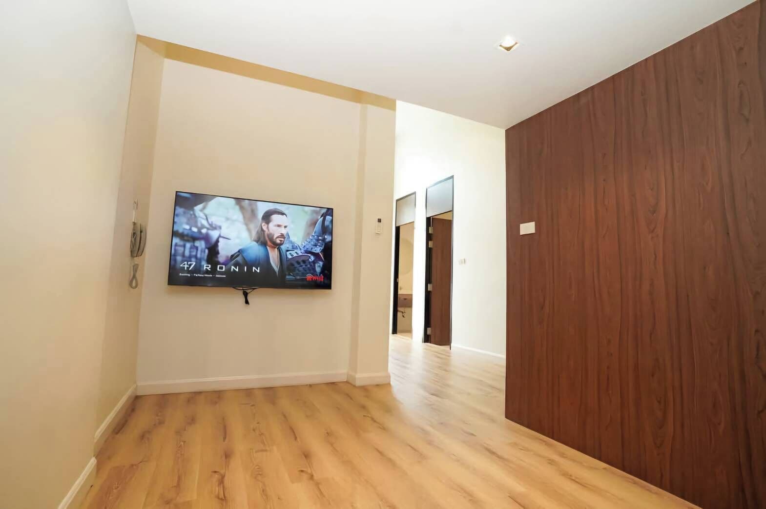 A hallway with a wooden floor, a mounted TV displaying a movie, and a wooden wall.