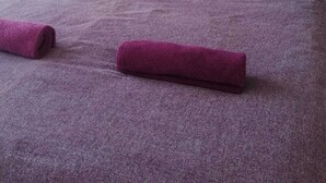 Una cama bien hecha con una colcha y almohadas moradas, una mesita de noche con una lámpara y cuadros en la pared.