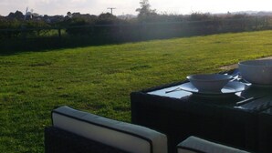 Un área de estar al aire libre con mesa y sillas, un campo cubierto de césped y un cielo despejado.