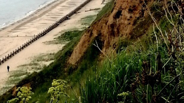 Un paisaje costero con playa, un acantilado y una valla de madera.