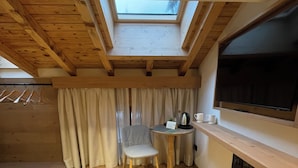 A cozy kitchen with a skylight, wooden beams, a small table with a chair, and a built-in oven. - Naturae Lodge (Alleghe)