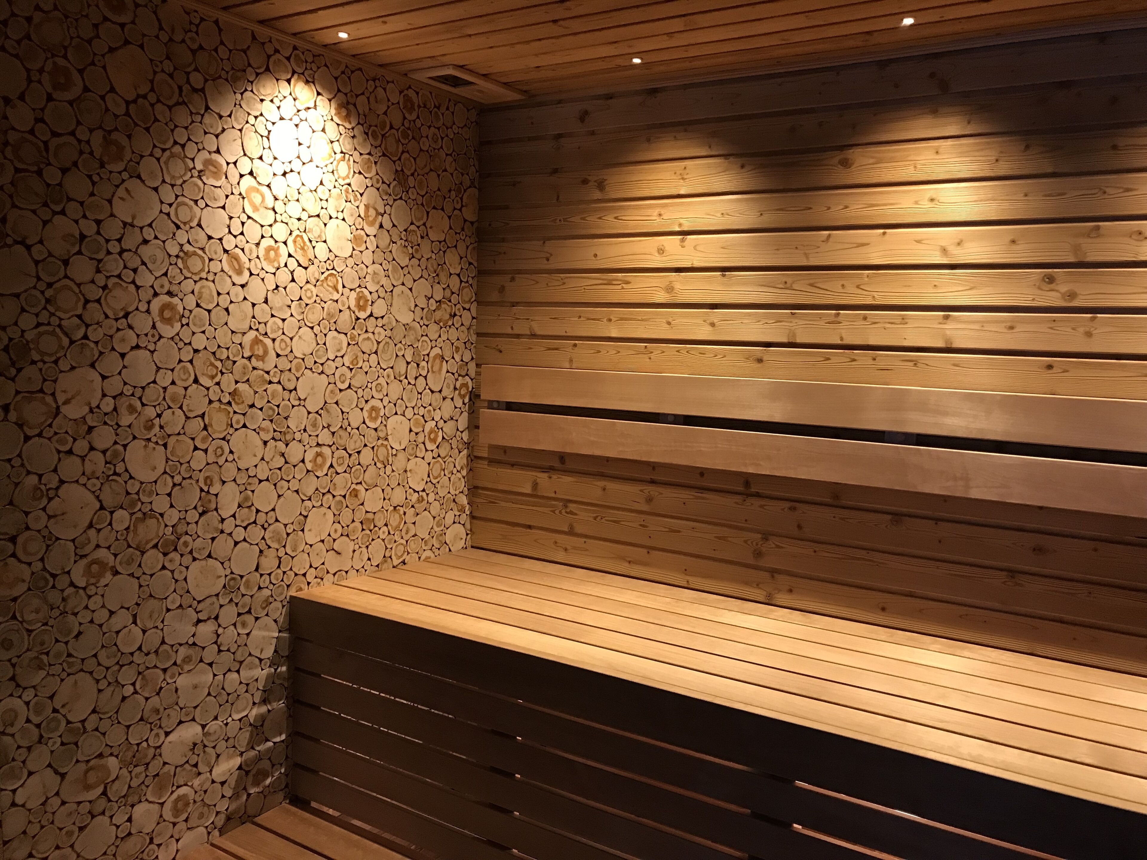 A sauna with a wooden bench and a wall covered with logs.