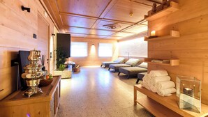 A wooden interior with a sauna, seating area, and a shelf with towels. - Naturae Lodge (Alleghe)