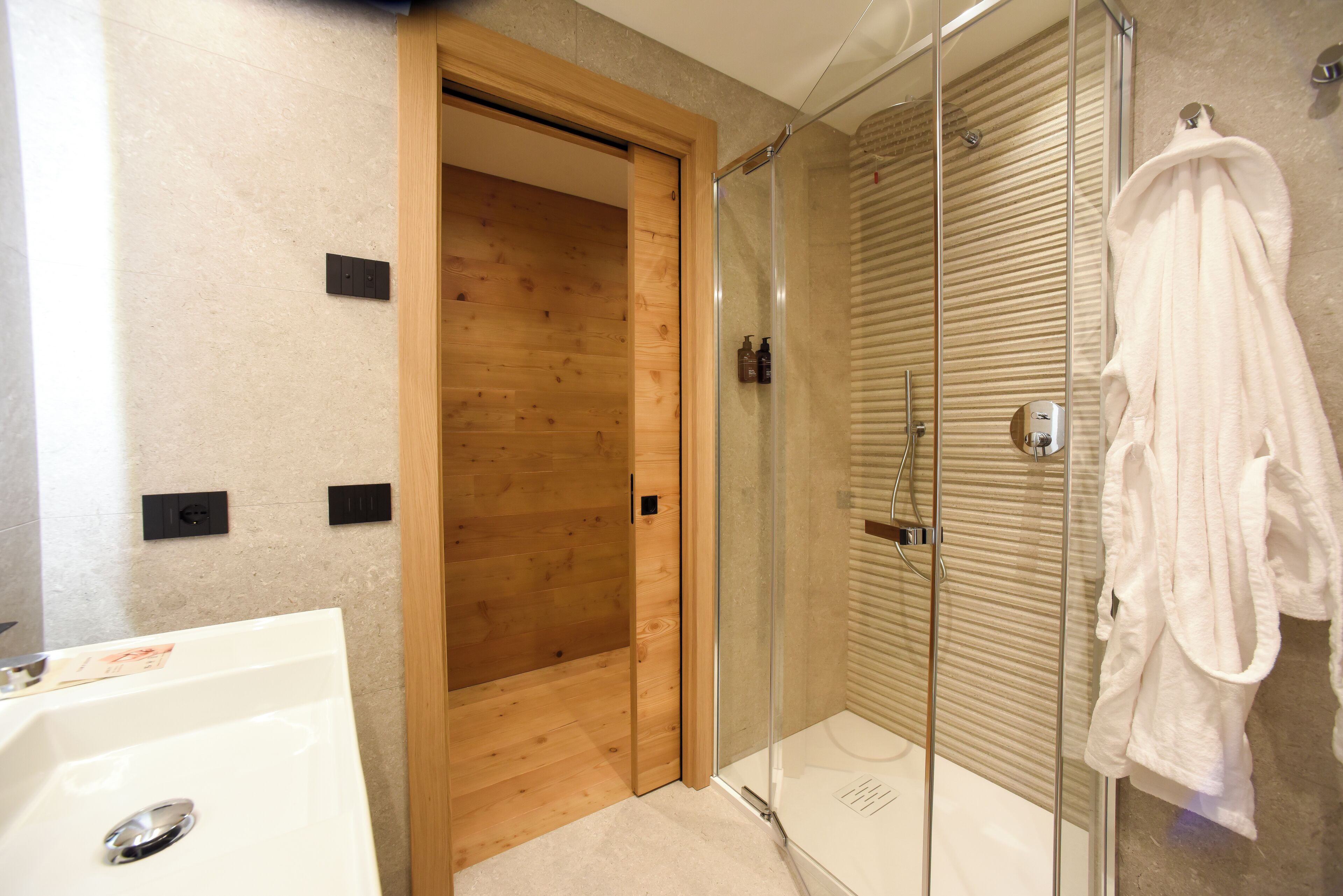 A modern bathroom with a glass-enclosed shower, a wooden door, and a white bathtub.