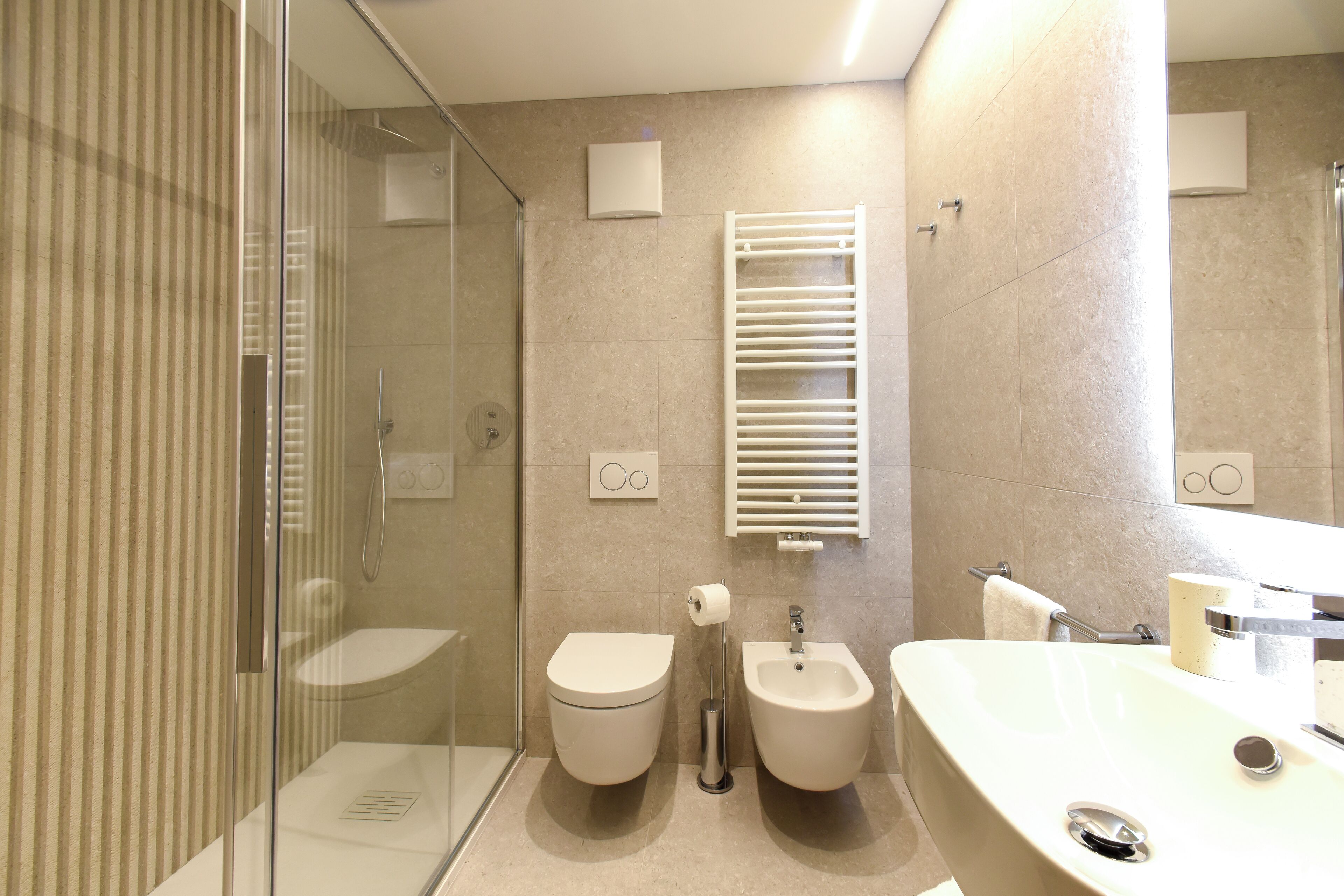 A modern bathroom with a glass shower enclosure, a toilet, a bidet, and a sink with a mirror.