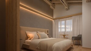 A modern bedroom with a large bed, a bedside table, a chair, and a window with curtains. - Naturae Lodge (Alleghe)