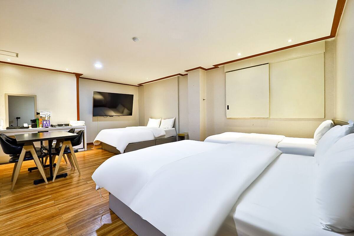 A hotel room with two beds, a desk, and a large TV.