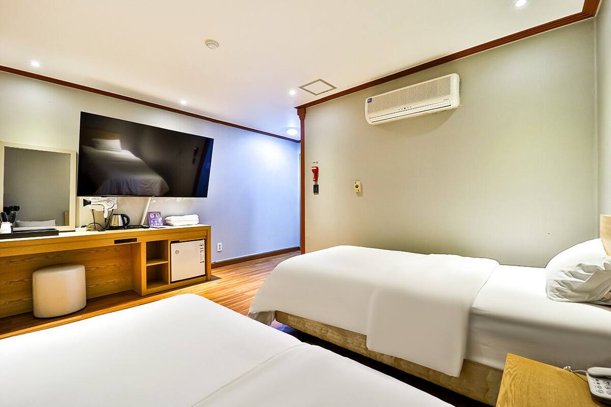 A hotel room with two beds, a TV, a desk with a computer, and a small cabinet.