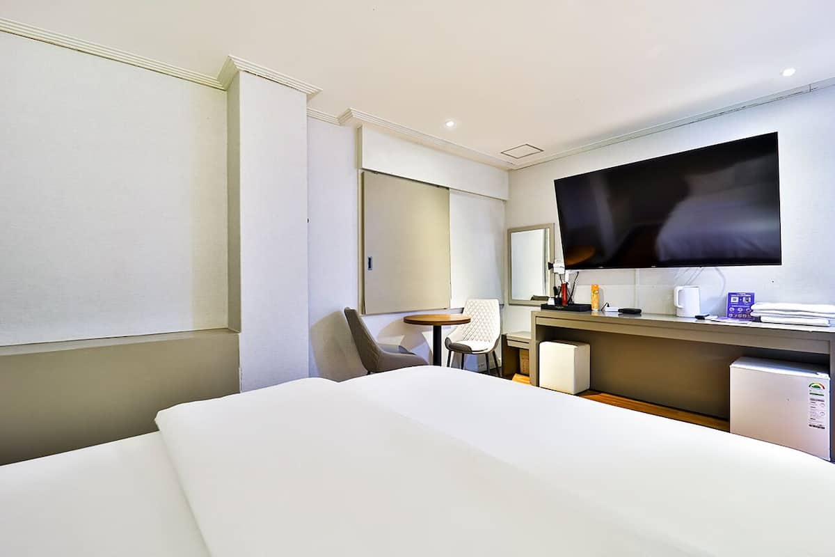 A hotel room with a bed, a desk, a chair, a television, and a mini-fridge.
