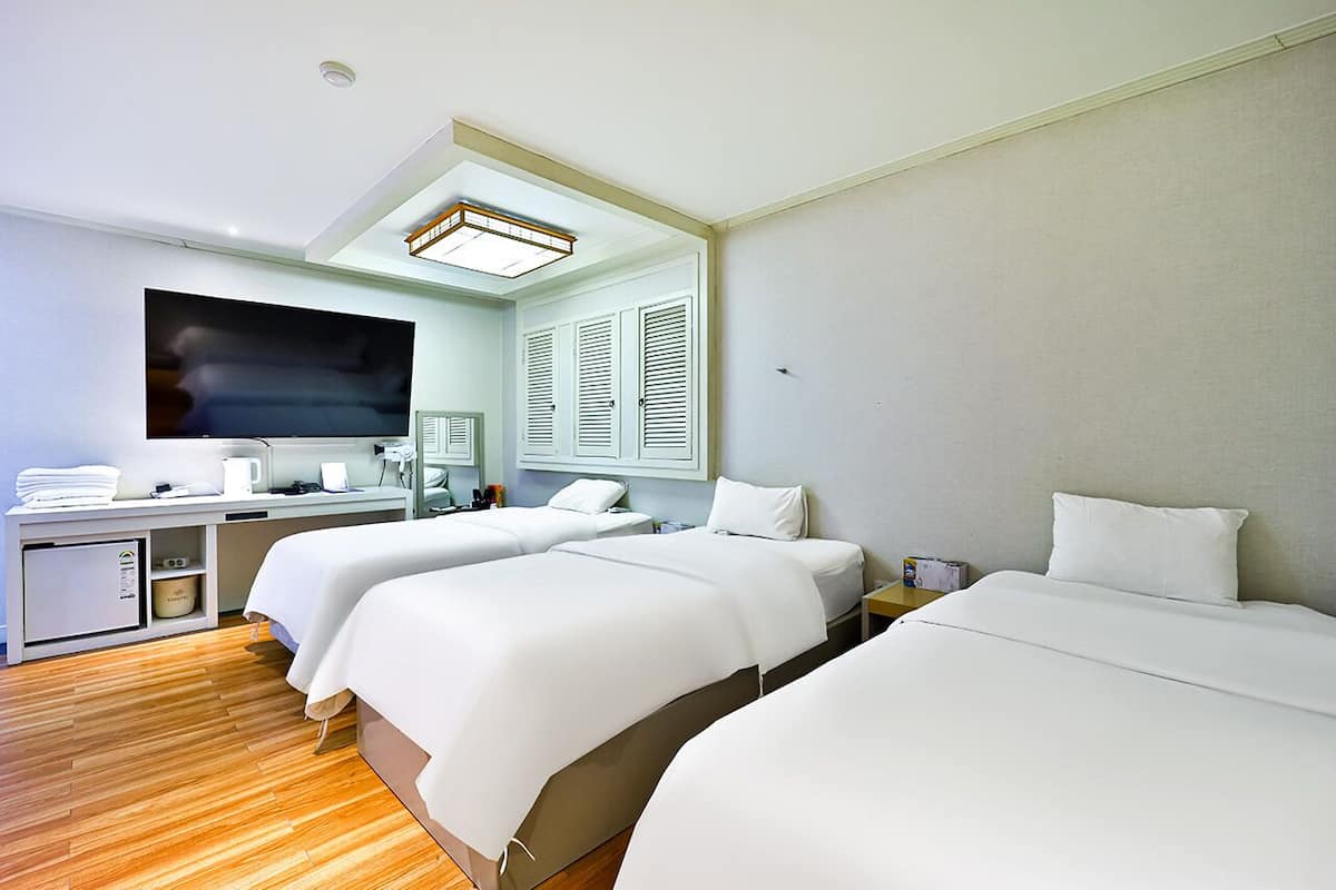 A hotel room with two beds, a desk, a television, and a window with shutters.
