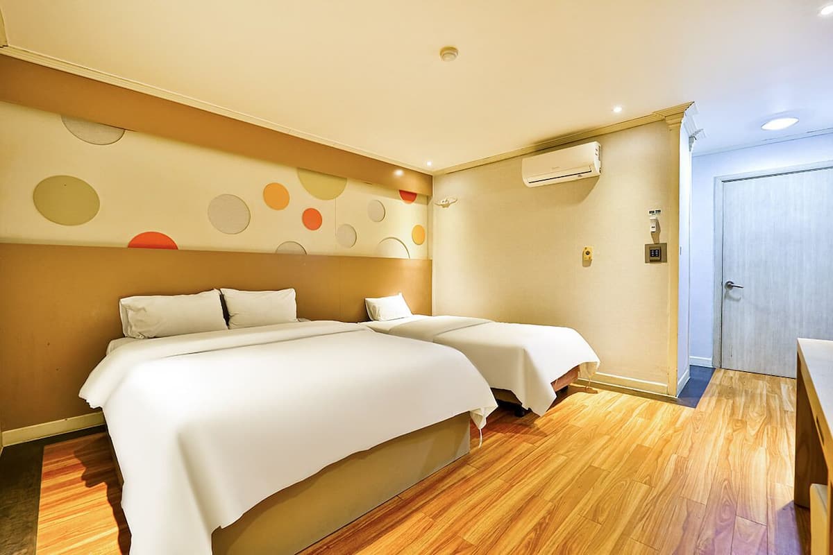 A hotel room with two beds, a wooden floor, a wall with circular patterns, and an air conditioning unit.