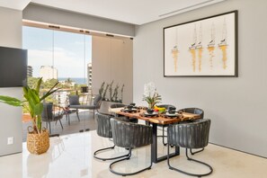 A modern dining area with a wooden table, black chairs, and a city view.