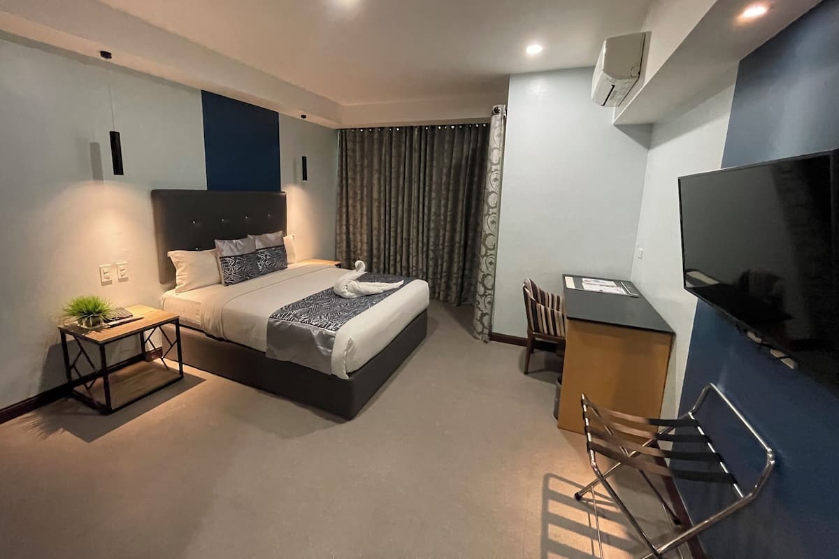 A modern hotel room with a bed, desk, chairs, and a TV.
