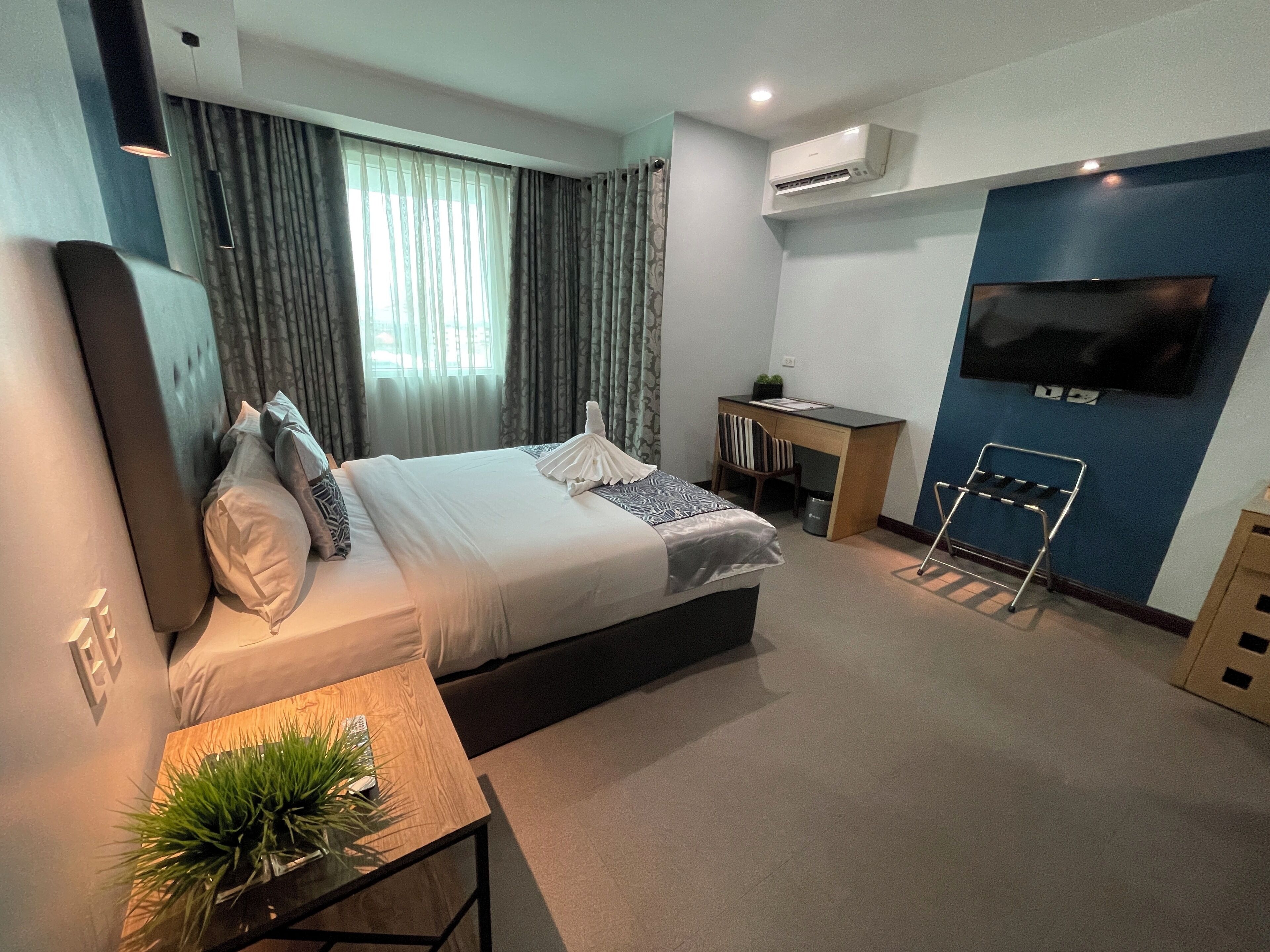 A modern hotel room with a large bed, a desk, a TV, and a small balcony.
