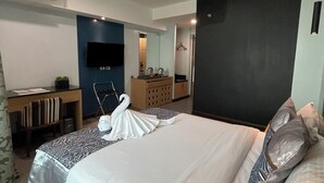 Una camera d'albergo moderna con un letto grande, una scrivania, una TV a schermo piatto e un bagno visibile attraverso una porta aperta.