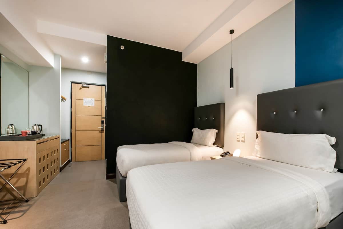 A hotel room with two beds, a wooden desk, and a dark accent wall.