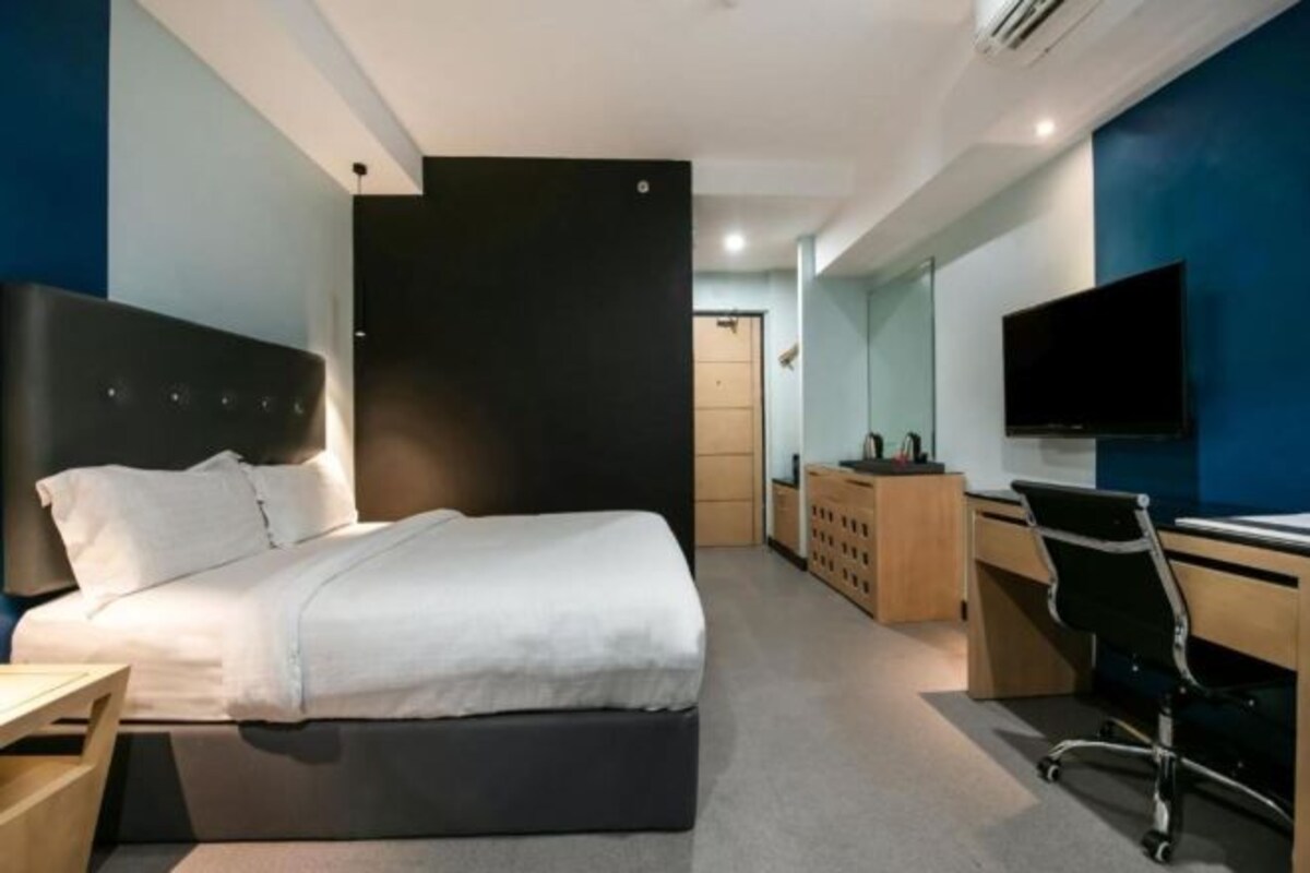 A modern hotel room with a bed, desk, chair, and a flat-screen TV.