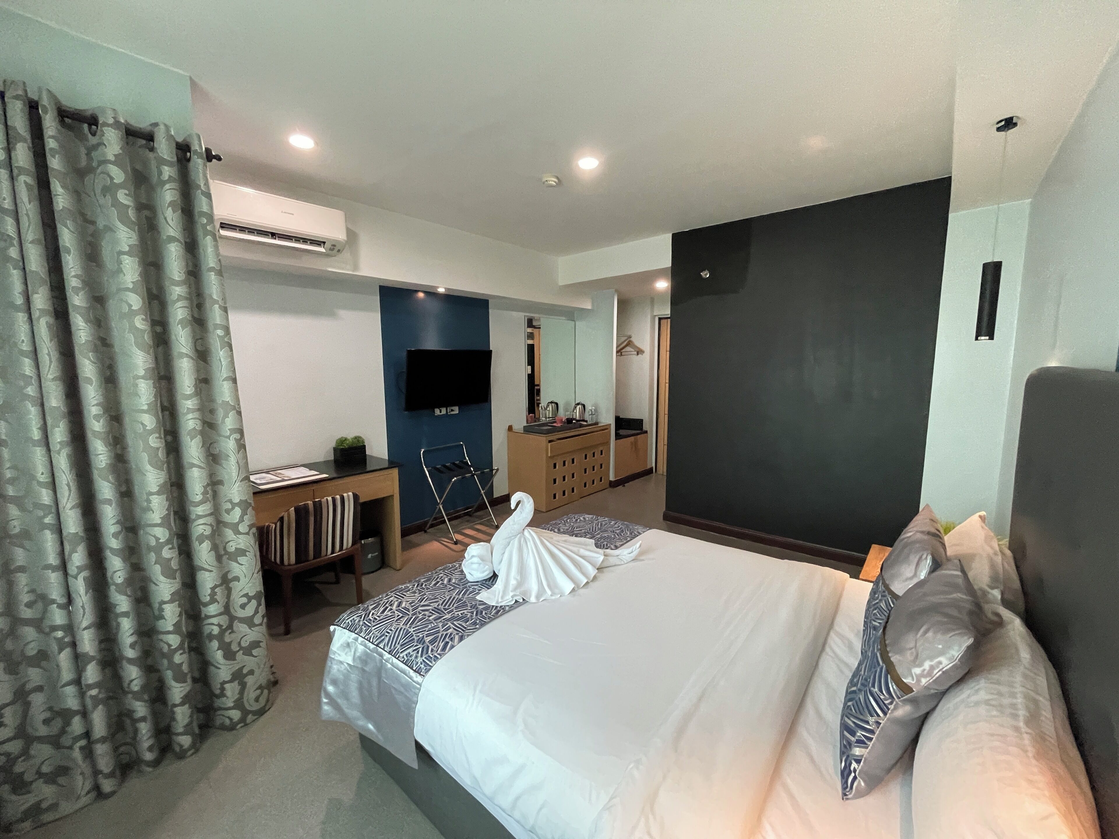 Quarto de hotel com cama, escrivaninha, televisão e guarda-roupa.