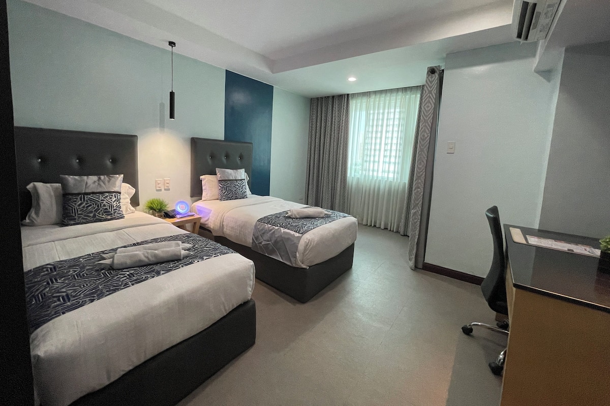 A modern hotel room with two beds, a desk, and a chair.