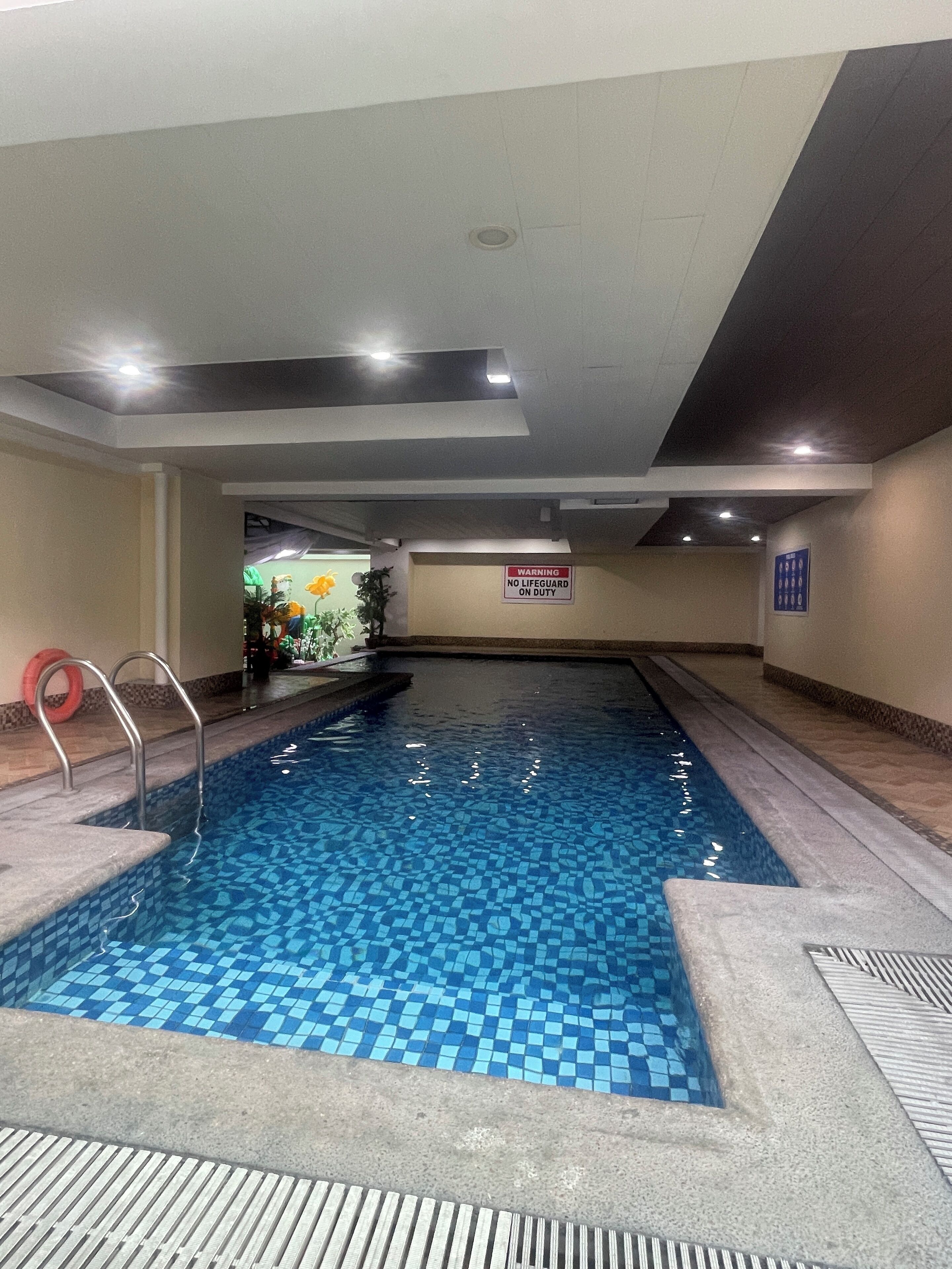 Una piscina interior amb sòl de rajola, una cadira de socorrista i un senyal de perill a la paret.