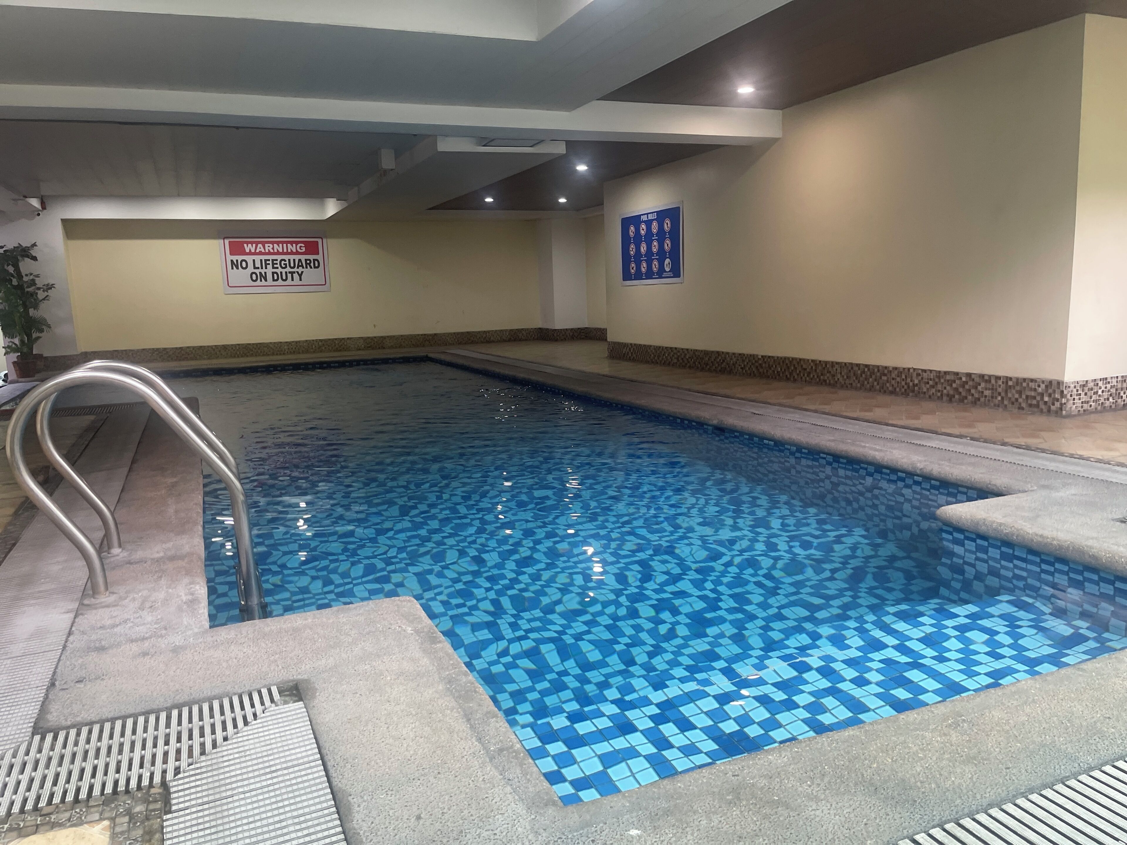 Una piscina interior con un letrero que indica 'No hay salvavidas de servicio', piso de baldosas y una silla de salvavidas.