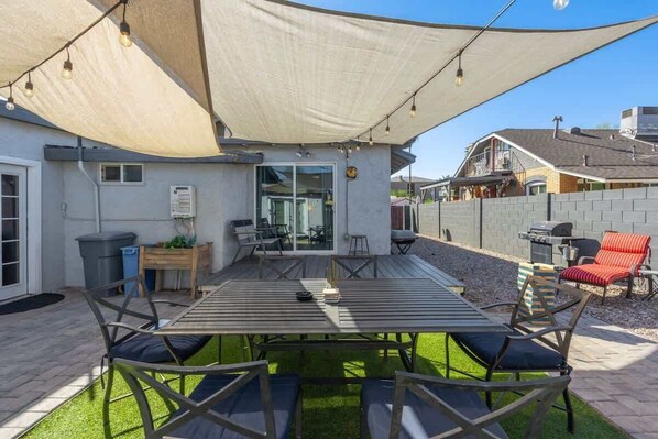 Een terras met een tafel, stoelen, een barbecue en een overdekte zithoek.