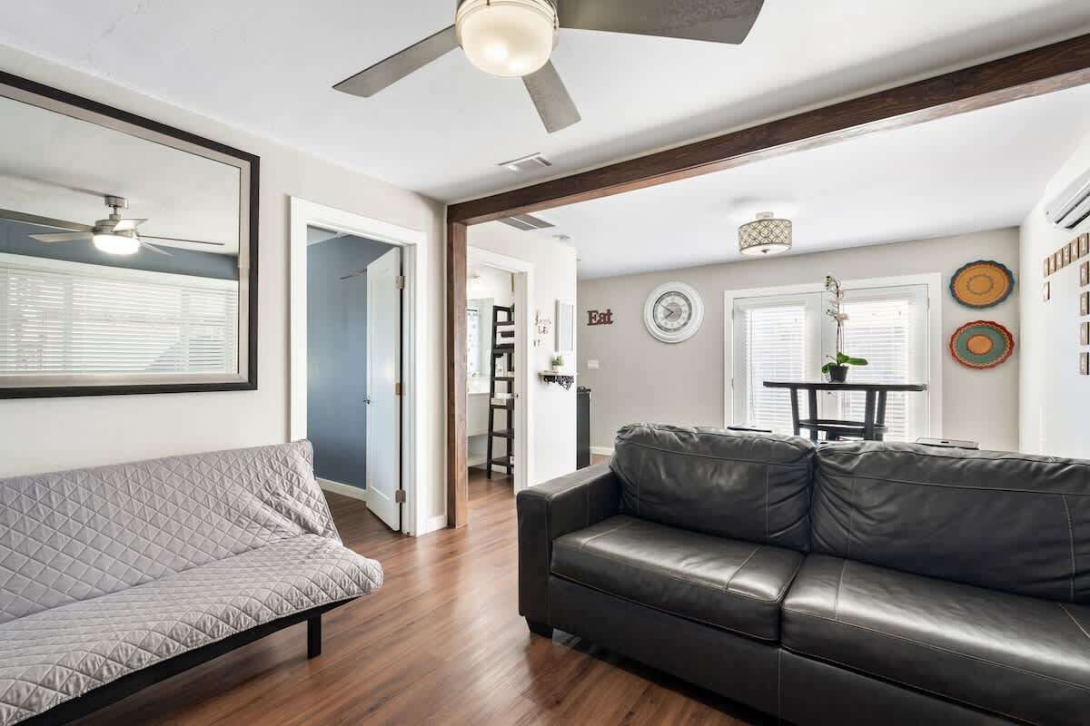 A living room with a sofa, a leather couch, a ceiling fan, and a dining area with a table and chairs.