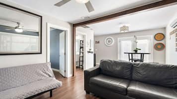 A living room with a sofa, a leather couch, a ceiling fan, and a dining area with a table and chairs.