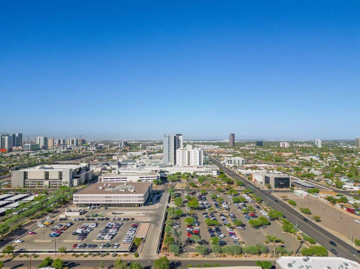 An aerial view of a cityscape with a large parking lot, several buildings, and a clear blue sky.