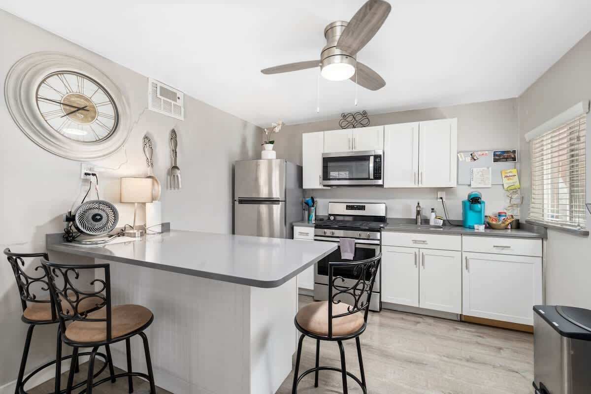 A modern kitchen with a central island, white cabinetry, a microwave, a stainless steel refrigerator, and a ceiling fan.