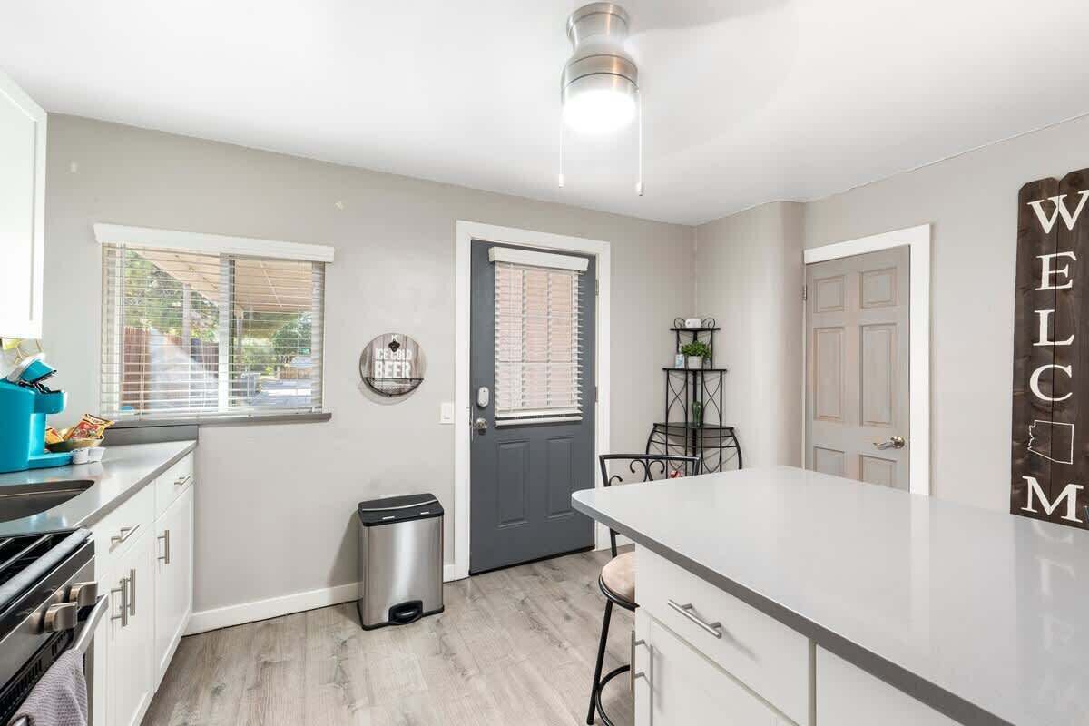 A modern kitchen with a grey door, a welcome sign, and a trash bin.