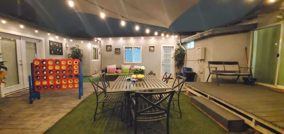 Un patio interior con una mesa redonda y sillas, una zona de estar con cojines y una pared decorativa con luces.