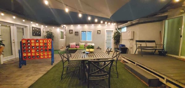 Un espace patio intérieur avec une table ronde et des chaises, un coin salon avec des coussins et un mur décoratif agrémenté de guirlandes lumineuses.