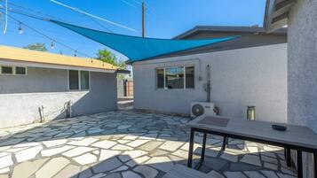 A patio area with a stone floor, a table, and a blue shade sail.