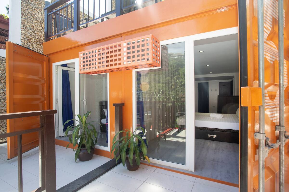 Een moderne hotelkamer met grote schuifdeuren, een balkon met een metalen hekwerk en potplanten.