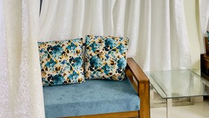 A room with a wooden sofa with floral cushions, a glass coffee table, and white curtains. - Chaubey Farms- Relax & Rejoice
- The best farm stay in Hyderabad (Chilipched)