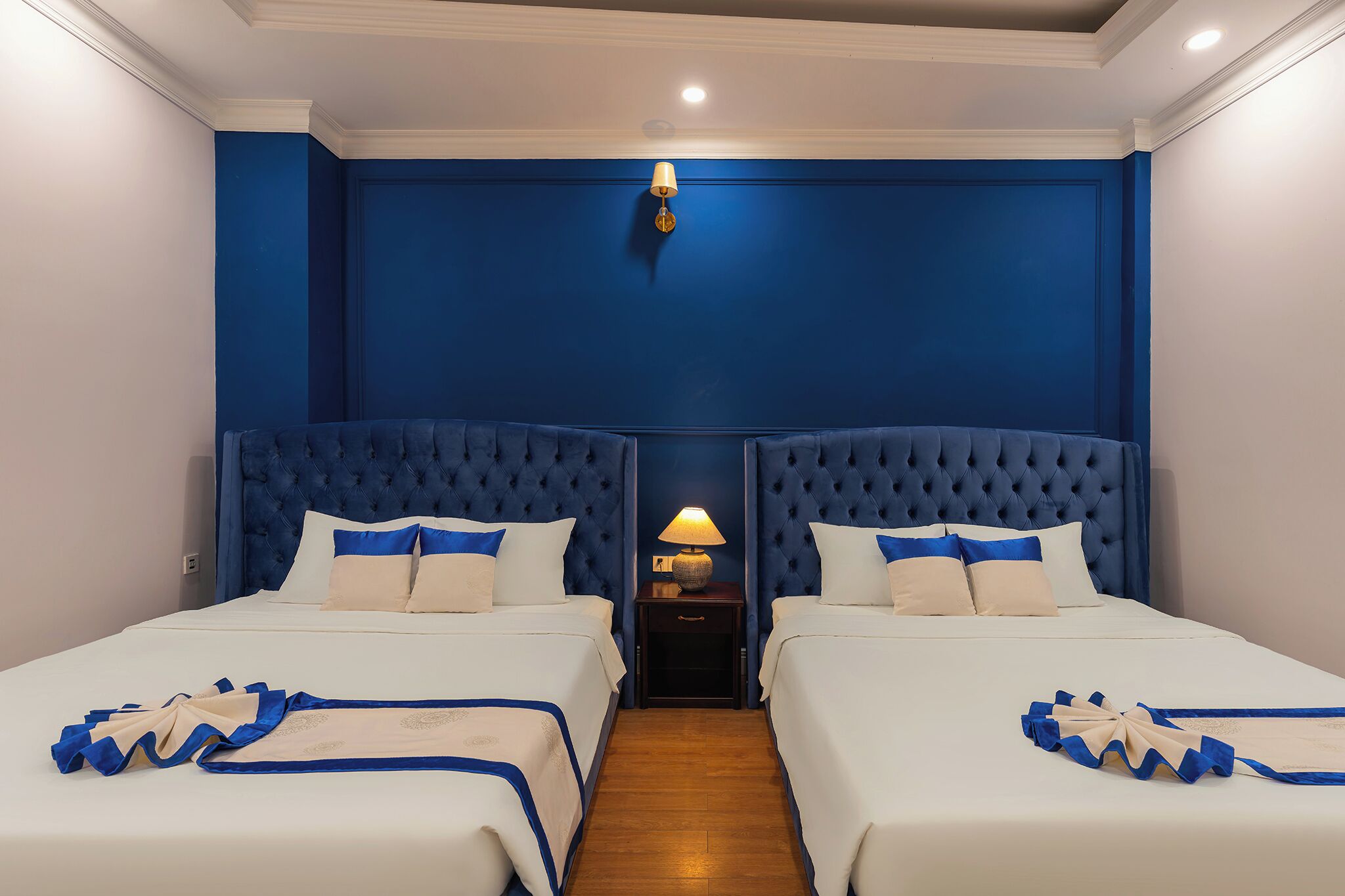 Une chambre d’hôtel avec deux lits, une table de chevet avec une lampe et un mur d’accent bleu.