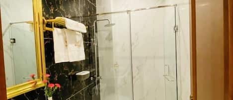 A modern bathroom with a marble vanity, a toilet, a glass-enclosed shower, and a large mirror with a gold frame.