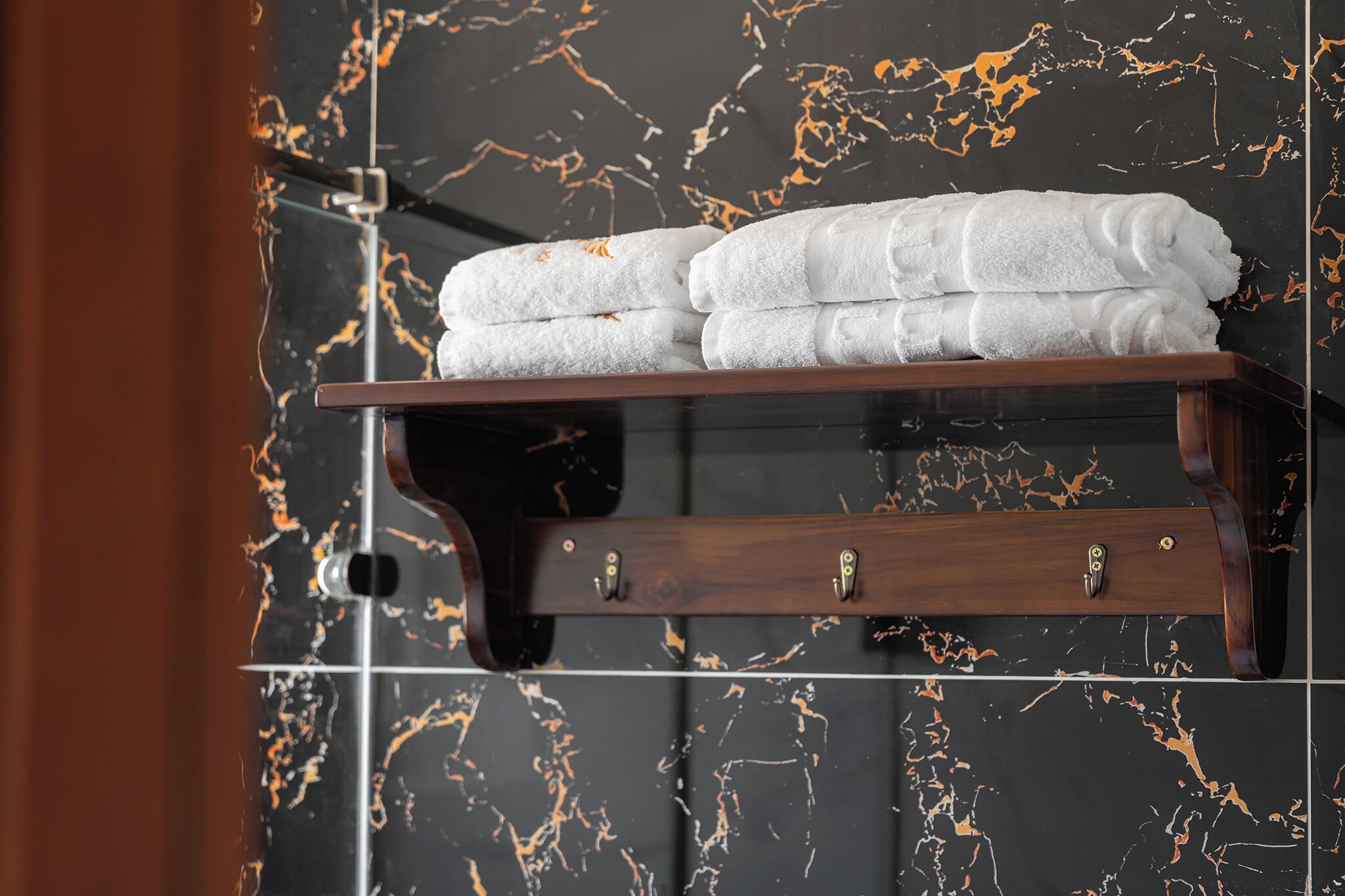 Une étagère en bois avec des serviettes blanches pliées, le tout adossé à un mur en marbre noir.