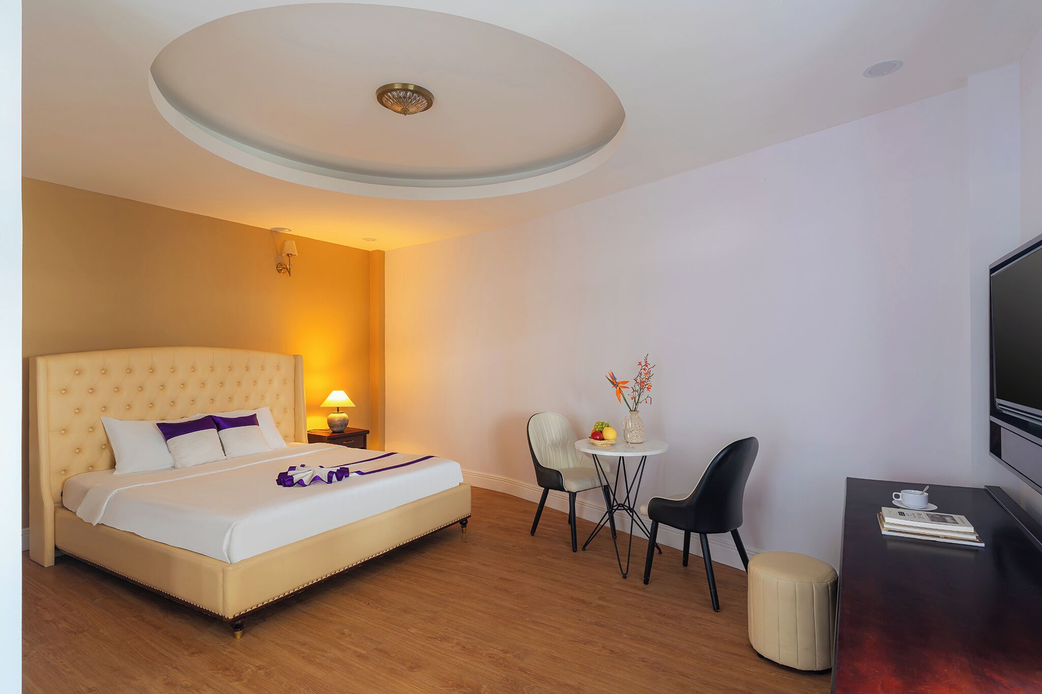 Hotellihuone, jossa on sänky, pieni pöytä tuoleineen, televisio ja lamppu.