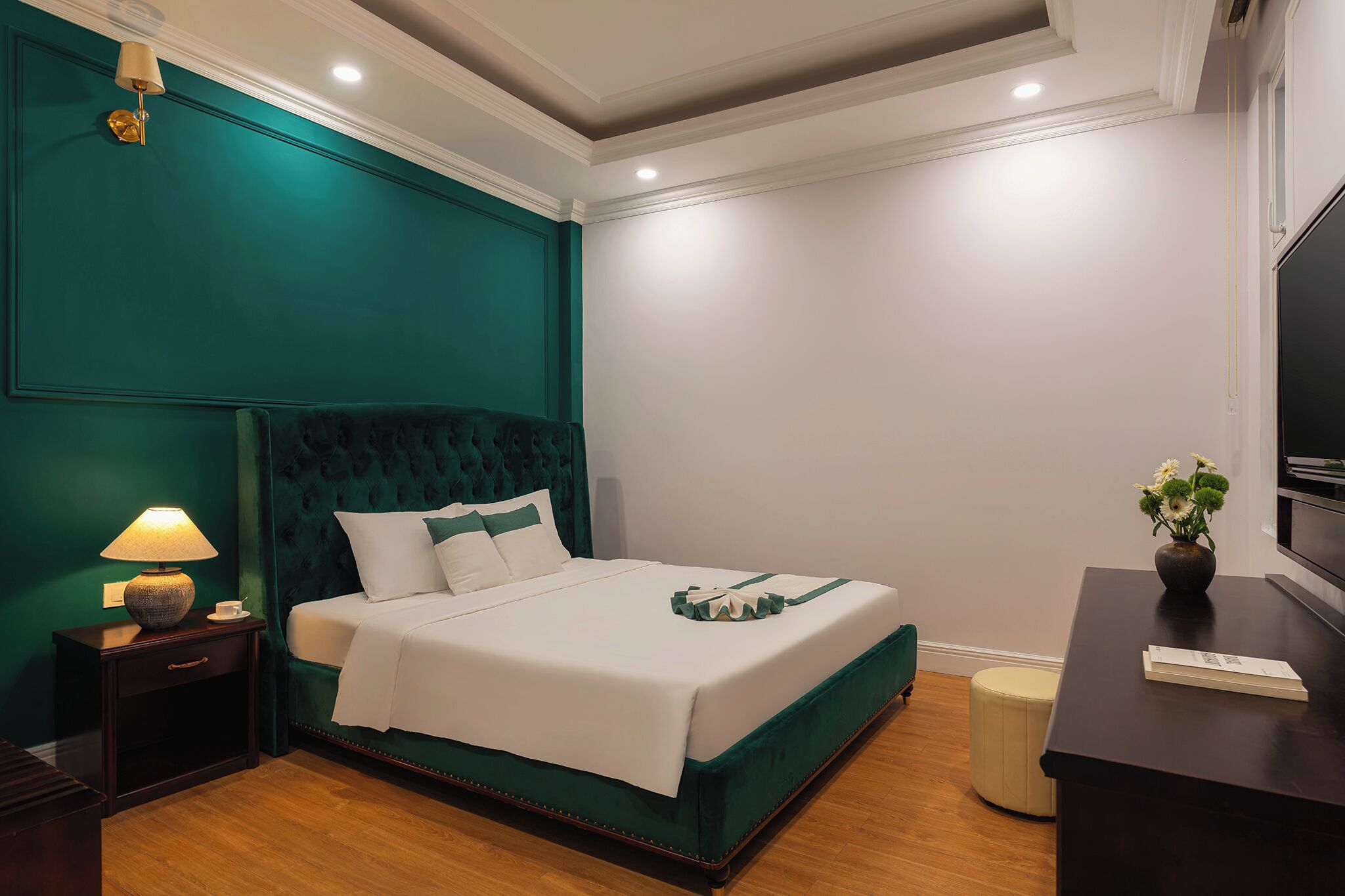 A neatly made bed with white linens, a teal accent wall, a bedside lamp, and a small bedside table.