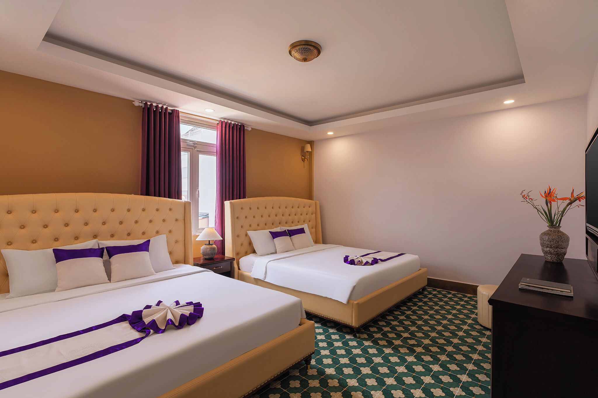 A hotel room with two beds, a TV, a desk, and a window with curtains.