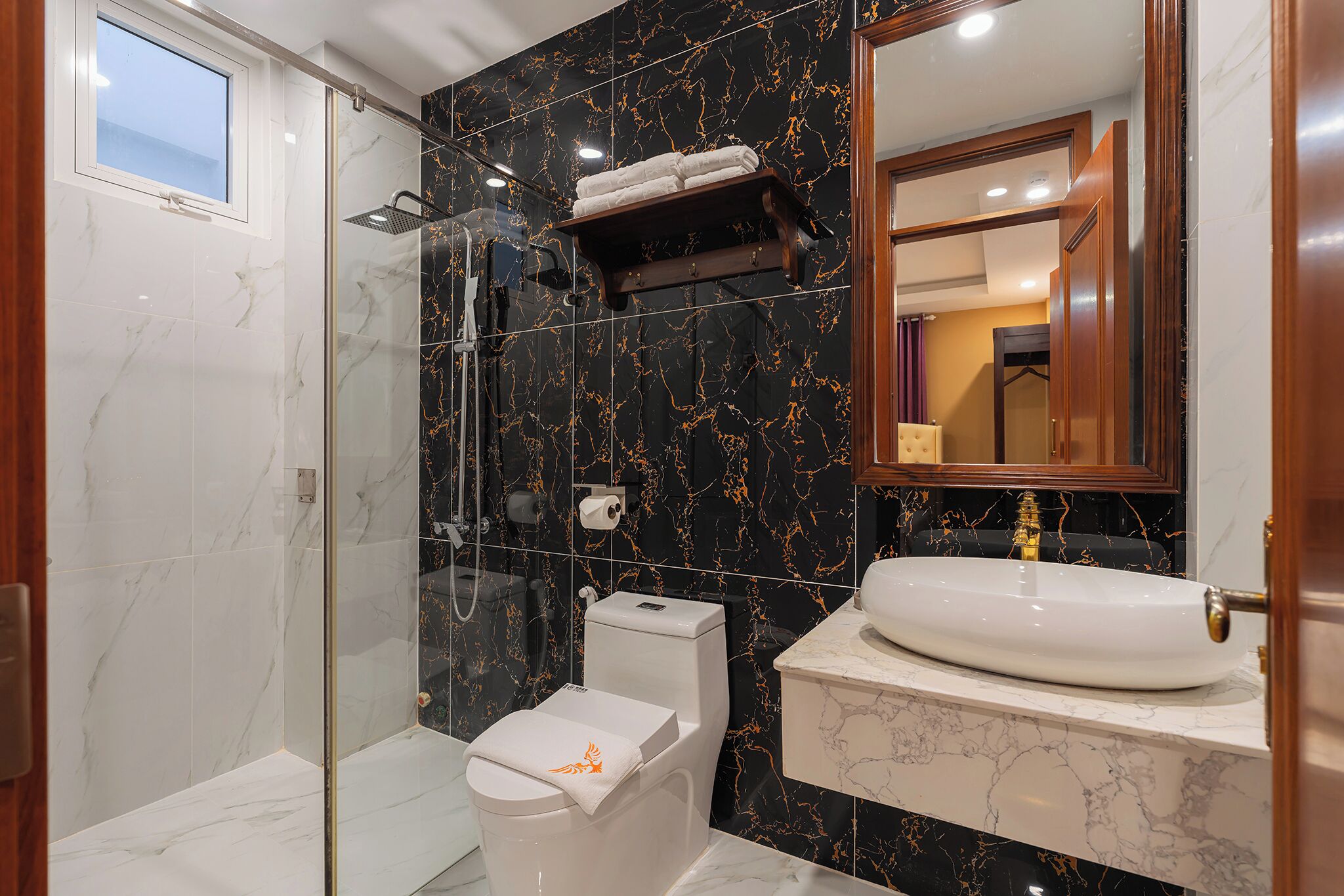A bathroom with a glass-enclosed shower, a white toilet, a marble sink, and a mirror above the sink.