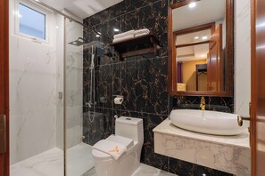 A bathroom with a glass-enclosed shower, a white toilet, a marble sink, and a mirror above the sink. - Peach Valley (Da Lat)
