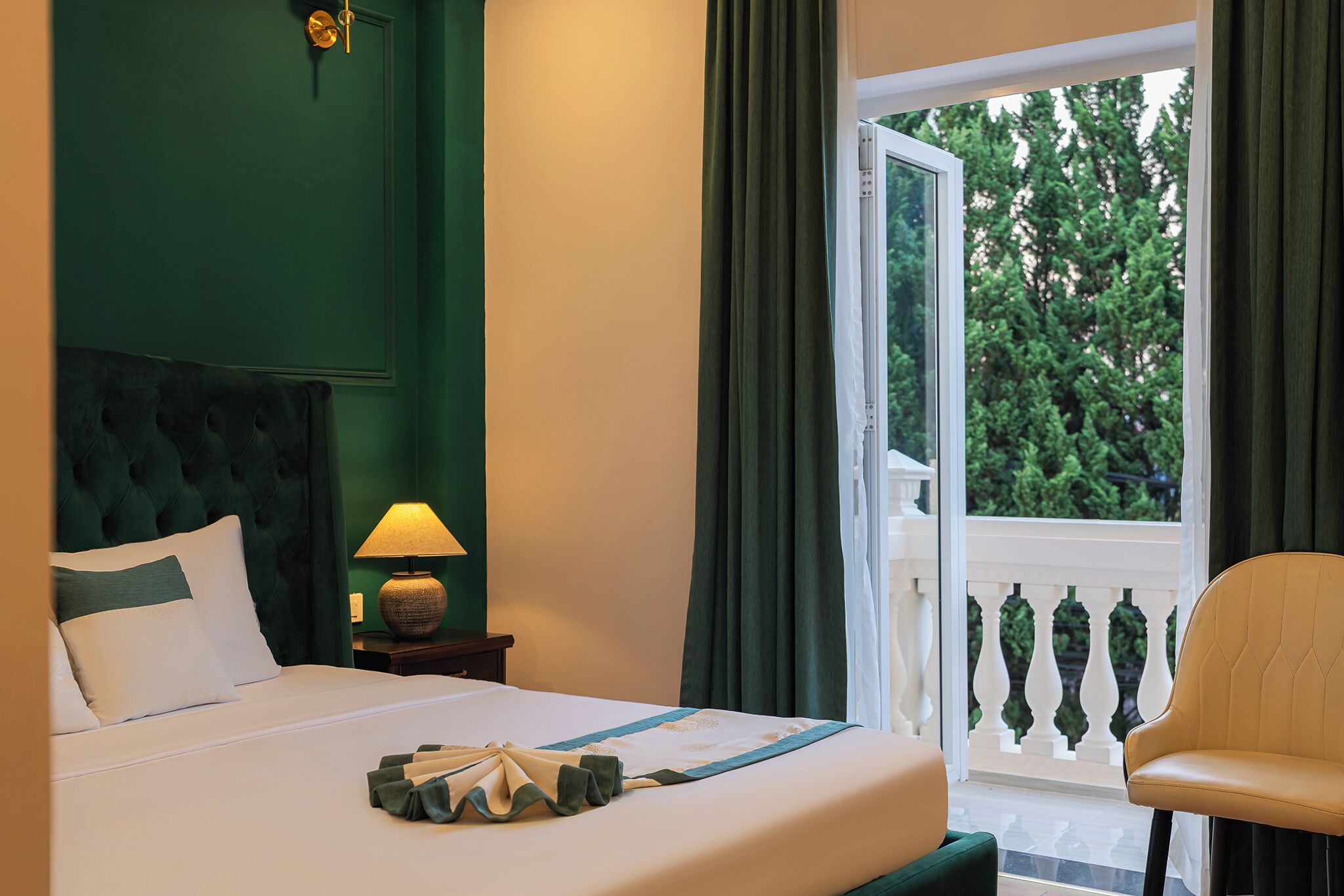 Une chambre d’hôtel avec un lit, une table de chevet avec une lampe, une chaise et un balcon doté d’une balustrade.