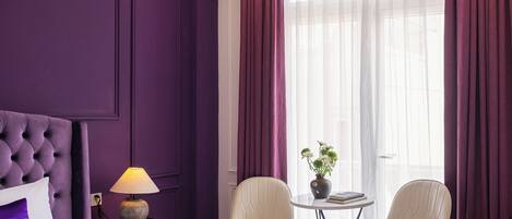Una habitación de hotel con una cama grande, dos sillas, una mesita y una ventana con cortinas.