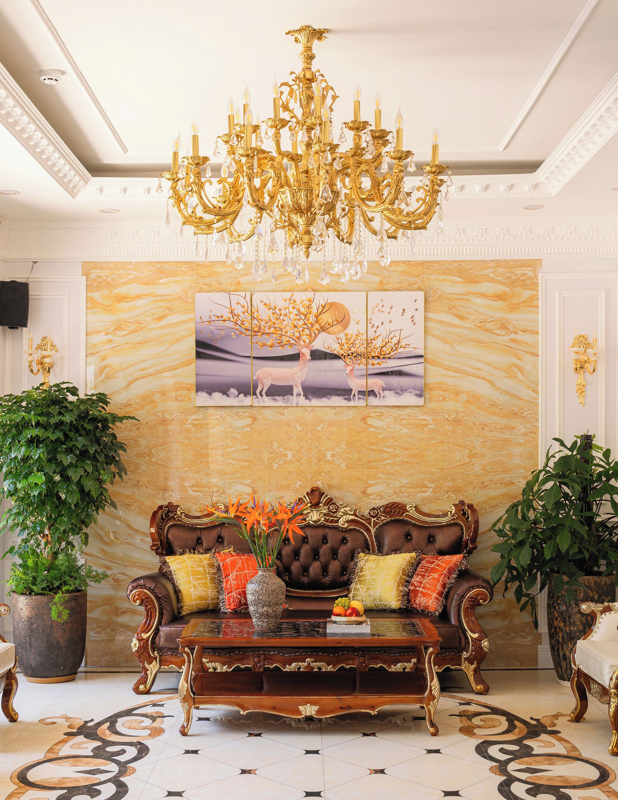 A luxurious room with a grand chandelier, a large sofa set, and a marble wall with a nature-themed painting.