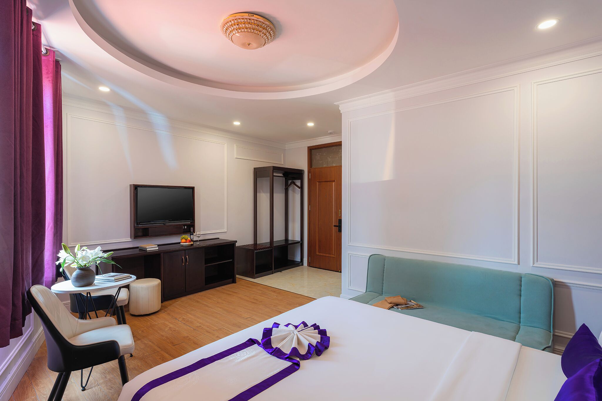 A hotel room with a bed, a desk with a TV, a seating area, and a wardrobe.